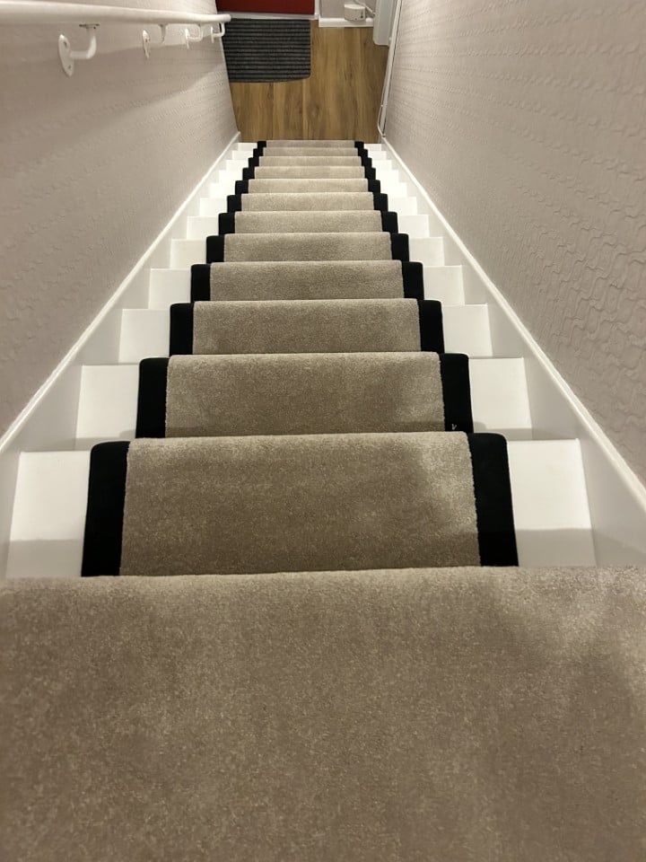 Beige carpeted staircase with black stair runners.